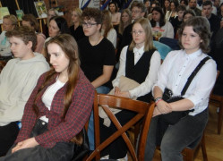 Grupa osób siedzi obok siebie. Osoby siedzą na krzesłach