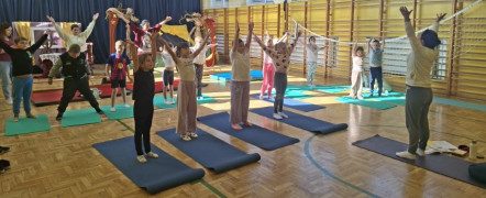 Dzieci podczas zajęć sportowych. Dzieci mają ręce uniesione do góry. Ćwiczą pod okiem instruktora 