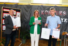 Chłopiec trzyma w ręku dyplom. Obok niego stoi kobieta i mężczyzna 