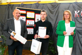 Chłopiec trzyma w ręku dyplom. Obok niego stoi kobieta i mężczyzna 