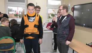 Grupa uczniów i mężczyzna. Jeden z uczniów ma założony kombinezon geriatyczny 