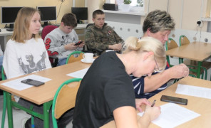 Dorośli i dzieci siedzą w szkolnych ławkach. Trwa szkolenie w ramach projektu Szkoła Międzypokoleniowa 