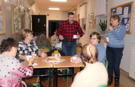 Dorośli i dzieci. Widoczne stoliki, na których znajdują się ciastka, kawa i herbata