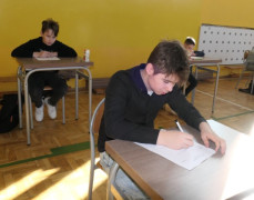 Chłopcy siedzą w ławkach i rozwiązują test