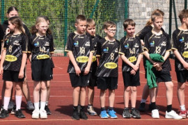 Dziewczęta i chłopcy w sportowych strojach stoją na płycie boiska obok siebie 