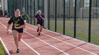 Trzy dziewczyny biegną na po bieżni znajdującej się na boisku sportowym 