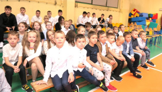 Grupa uczniów siedząca na ławeczkach 