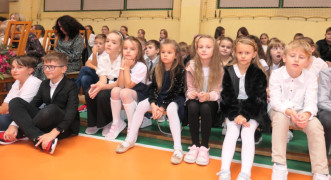 Grupa uczniów siedząca na ławeczkach 