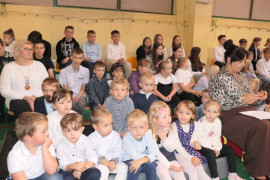 Grupa uczniów siedząca na ławeczkach 
