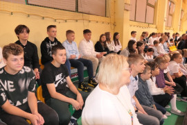 Grupa uczniów siedząca na ławeczkach 