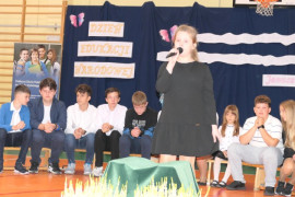 Uczniowie podczas występu. Jedna z dziewczynek stoi i trzyma w ręku mikrofon 