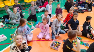 Dzieci siedzą na podłodze, na której znajdują się klocki lego