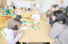 Dzieci siedzą przy stoliku i układają klocki lego towarzyszy im nauczycielka 
