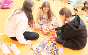 Trzy nastolatki siedzą na podłodze i układają klocki lego
