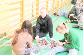 Dwie dziewczyny i chłopiec siedzą na podłodze i układają klocki lego