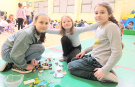 Trzy dziewczynki siedzą na podłodze i układają klocki lego