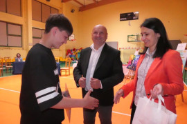 Kobieta wręcza chłopcu nagrodę. Obok stoi mężczyzna 