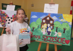 Dziewczynka stoi przy pracy konkursowej. W dłoniach trzyma dyplom 