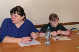 Kobieta i dziewczynka siedzą obok siebie przy stole. Obie robią ozdoby