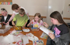 Dorośli i dzieci siedzą przy stole. Trwają warsztaty decoupage