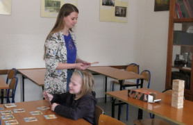 Kobieta i dziewczynka. Kobieta stoi obok ławki, dziewczynka siedzi w ławce