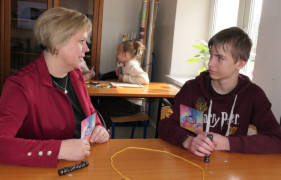 Kobieta siedzi w ławce naprzeciwko chłopca. Osoby rozmawiają ze sobą 