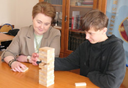 Kobieta i chłopiec siedzą obok siebie w szkolnej ławce. Osoby układają piramidę z klocków