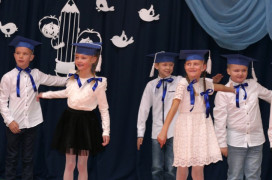 Grupa dzieci w granatowych biretach na głowie. Dzieci występują na akademii szkolnej 