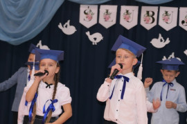 Dziewczynka i chłopiec w granatowych biretach na głowie. Dzieci biorą udział w szkolnej akademii 