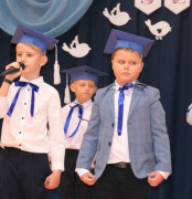 Trzej chłopcy w granatowych biretach na głowie. Dzieci uczestniczą w szkolnej akademii 