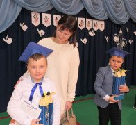 Dwaj chłopcy w granatowych biretach na głowie. Obok jednego z nich stoi kobieta 