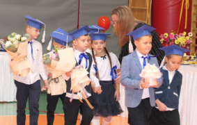 Grupa dzieci w granatowych biretach na głowie. Dzieci trzymają w dłoniach kwiaty