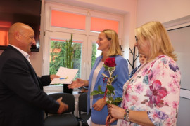 Dwie kobiet i mężczyzna. Mężczyzna wręcza kobiecie dokumenty i różę. Moment awansu zawodowego