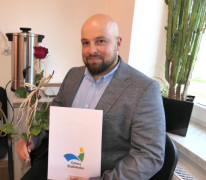 Uśmiechnięty mężczyzna siedzący na krześle i trzymający w dłoniach dokumenty 