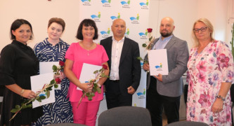 Cztery kobiety i dwóch mężczyzn. Trzy kobiety i mężczyzna trzymają w ręku dokumenty i czerwone róże 