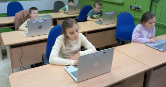 Uczniowie siedzą w szkolnych ławkach. Uczniowie korzystają z laptopów 