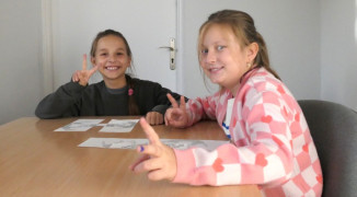 Dwie dziewczynki siedzą w szkolnej ławce. Dziewczynki uczestniczą w warsztatach. 