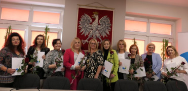 Grupa kobiet stojących na tel godła Polski. Panie trzymają w ręku czerwone róże