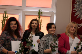 Cztery kobiety stojące na tle okna. Panie trzymają w ręku róże 