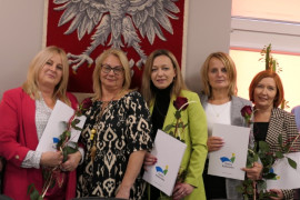 Pięć kobiet stojących na tle godła Polski. Panie trzymają w ręku czerwone róże