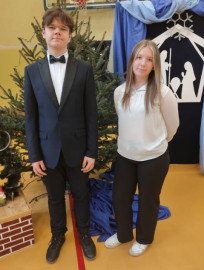 Dziewczyna w białej bluzce i ciemnych spodniach oraz chłopiec w garniturze stoją obok siebie