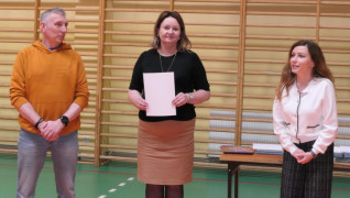 Dwie kobiety i mężczyzna stoją obok siebie. Jedna z kobiet trzyma w ręku dokumenty