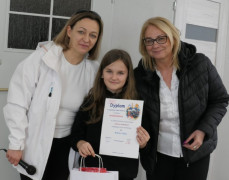 Dwie kobiety i dziewczynka. Dziewczynka trzyma w ręku dyplom 