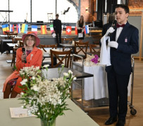 Dziewczyna w pomarańczowej garsonce siedzi na krześle. Chłopak w czarnym garniturze stoi obok niej. Dziewczyna wcieliła się w rolę angielskiej królowej, natomiast chłopak wystąpił jako szarmancki lokaj. 