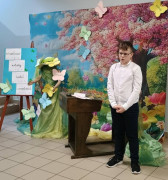 Chłopiec w białej bluzce i czarnych spodniach stoi i recytuje wiersz 