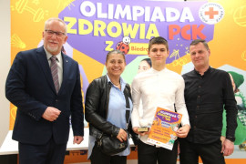 Cztery osoby: kobieta, dwóch mężczyzn i chłopiec stoją obok siebie. Chłopiec trzyma w ręku dyplom 