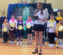 Dziewczynka prowadzi szkolną akademię. Za nią stoją inni uczniowie 