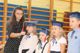 Grupa dzieci stojąca obok siebie. Jedna z dziewczynek mówi do mikrofonu