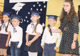 Grupa uczniów stojąca obok siebie. mniejsze dzieci mają na głowach granatowe birety 