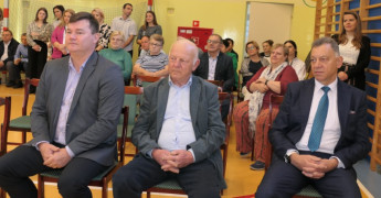 Grupa osób siedząca na krzesłach. Na pierwszym planie trzech mężczyzn 